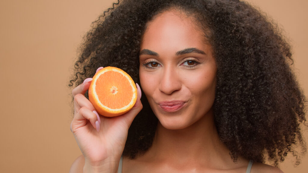 Mulher segurando uma metade de laranja, rica em vitamina C.