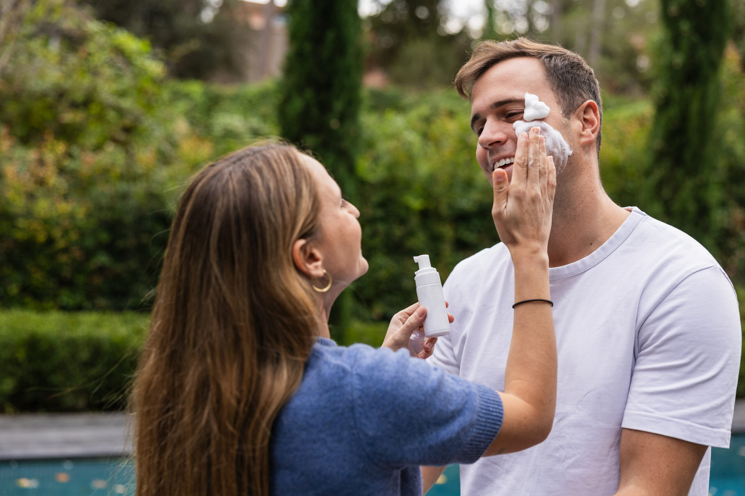 Mulher aplicando espuma esfoliante no rosto do homem ao ar livre